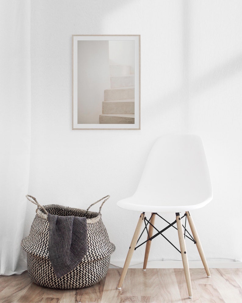 Peut inclure: Une chaise blanche avec des pieds en bois et un si&egrave;ge en osier noir se trouve devant un mur blanc avec une photographie encadr&eacute;e d'un escalier blanc. Un panier en osier noir et blanc se trouve sur le sol &agrave; c&ocirc;t&eacute; de la chaise.
