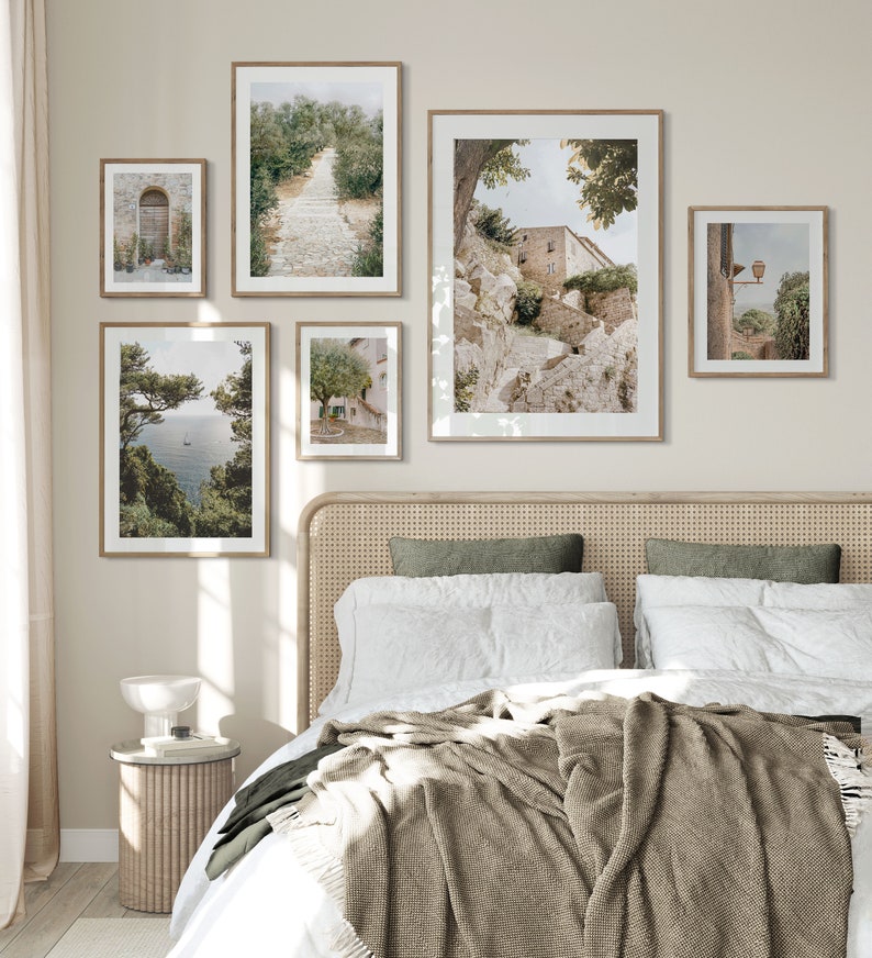 Pode incluir: Um quarto com uma cama com um edredom branco e uma manta de l&atilde; marrom. A cabeceira &eacute; feita de vime tecido. H&aacute; cinco quadros emoldurados na parede acima da cama, todos representando cenas de uma pequena cidade na It&aacute;lia. Os quadros s&atilde;o de tamanhos diferentes e est&atilde;o dispostos em um padr&atilde;o sim&eacute;trico.