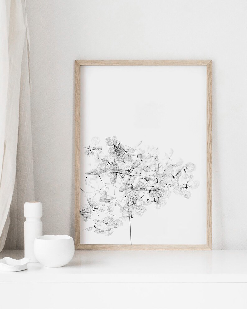 May include: A black and white framed print of a delicate floral design. The print features a cluster of small, intricate flowers with a stem extending down the center. The print is set against a white background.