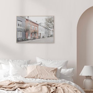 May include: A framed photograph of a row of colorful houses with a tree in the background. The houses are painted in shades of gray, pink, and white. There are bicycles parked in front of the houses.
