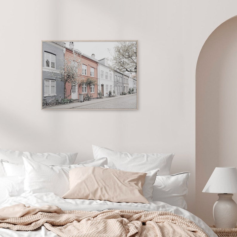 May include: A framed photograph of a row of colorful houses with a tree in the background. The houses are painted in shades of gray, pink, and white. There are bicycles parked in front of the houses.