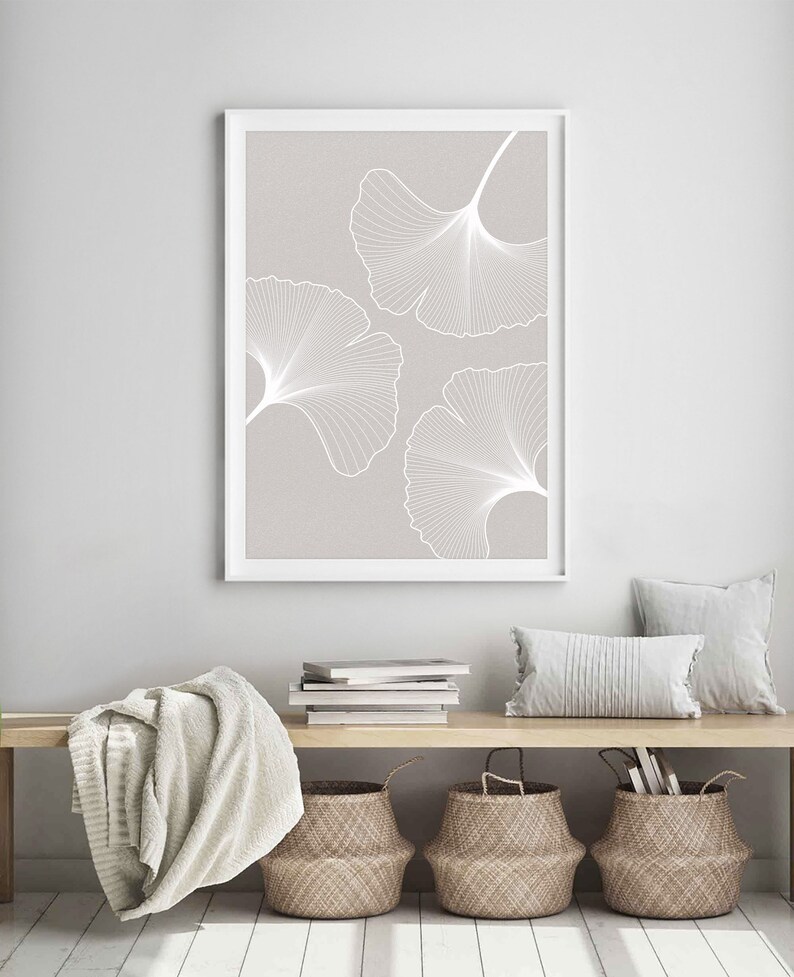 Puede incluir: Una impresi&oacute;n art&iacute;stica enmarcada con tres contornos de hojas de ginkgo blancas sobre un fondo gris claro. La obra de arte se exhibe sobre un banco de madera con cestas tejidas, cojines y una manta doblada, creando una est&eacute;tica minimalista inspirada en la naturaleza.