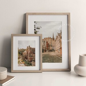 May include: Two framed photographs of cityscapes in Edinburgh, Scotland. The larger photo shows a street lined with historic buildings, while the smaller photo shows a close-up of a building with a red roof.