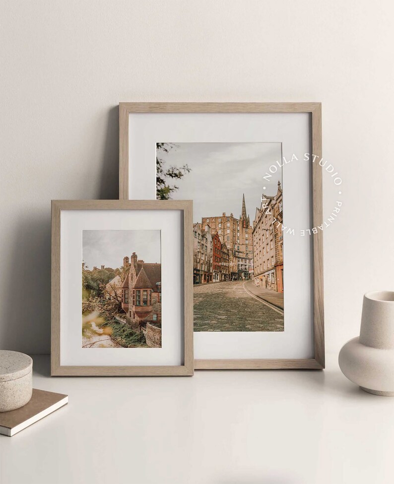 May include: Two framed photographs of cityscapes in Edinburgh, Scotland. The larger photo shows a street lined with historic buildings, while the smaller photo shows a close-up of a building with a red roof.