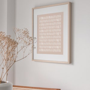 May include: A framed abstract print with a light brown background and white lines. The print is in a simple wooden frame.