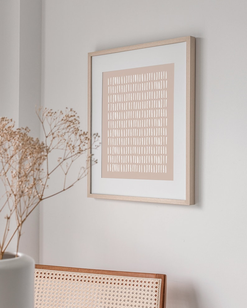 May include: A framed abstract print with a light brown background and white lines. The print is in a simple wooden frame.