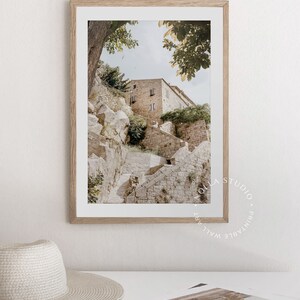 May include: A framed photograph of a stone building with steps leading up to it. The building is surrounded by trees and greenery. The photo is in a light wood frame.
