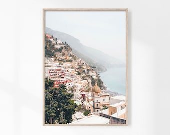 May include: A photograph of a coastal town built into a hillside with a church at the bottom of the frame. The town is a mix of white and red buildings with a blue ocean in the background.