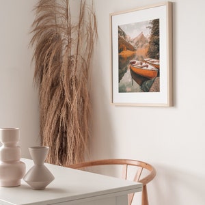 May include: A framed photograph of a lake surrounded by mountains with two wooden boats docked on the water. The photo is in a light wood frame and is hanging on a white wall.
