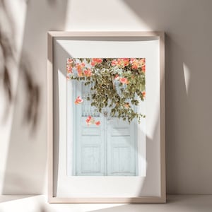 May include: A framed photograph of a white wooden door with pink flowers growing over it. The door is double-doored and has a simple design.