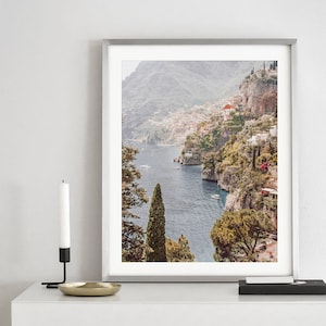 May include: A framed photograph of a coastal town nestled on a hillside overlooking a blue body of water. The town is surrounded by lush green trees and the water is dotted with boats.