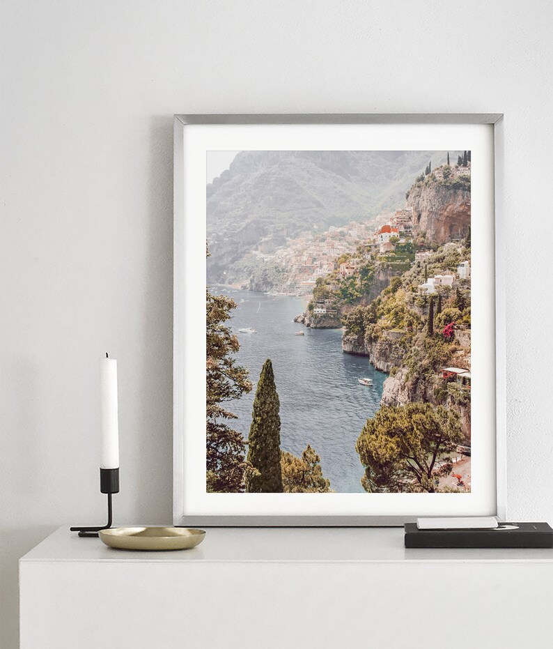 May include: A framed photograph of a coastal town nestled on a hillside overlooking a blue body of water. The town is surrounded by lush green trees and the water is dotted with boats.