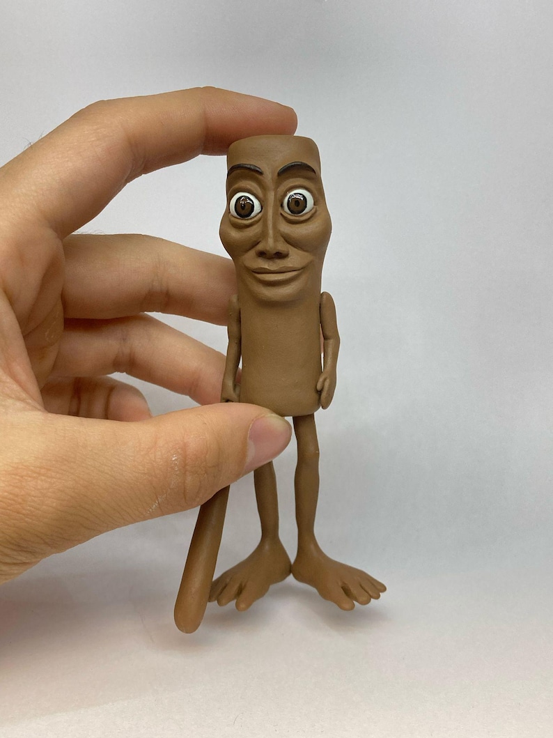 May include: A brown clay figurine of a person with large eyes and a wide smile. The figurine has long legs and feet.