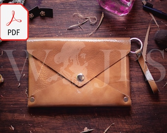 May include: A tan leather envelope clutch with a silver snap closure and a detachable strap. The clutch is on a wooden surface.