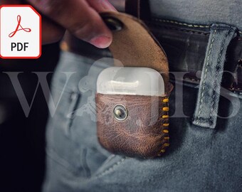 May include: A brown leather case with yellow stitching for AirPods, with a white plastic case inside. The case is being placed in a back pocket of jeans.