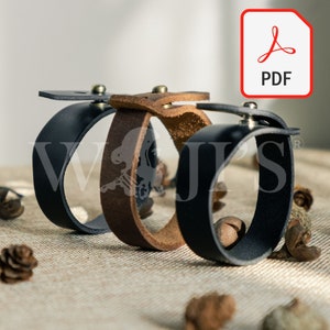 May include: Three leather bracelets with metal clasps. The bracelets are brown, black, and black with a brown accent. The bracelets are arranged in a stack on a light brown surface.
