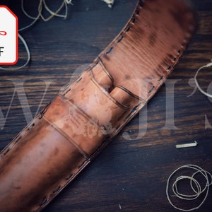 Op de afbeelding: Een bruin leren pennenetui met stiksels, open om twee vakken voor pennen te laten zien. Het etui ligt op een houten oppervlak.