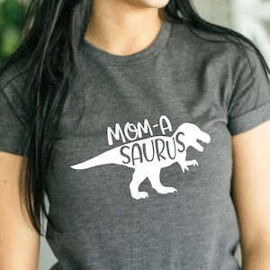 May include: Gray t-shirt with a white dinosaur graphic and the text "MOM-A-SAURUS" printed on the front.