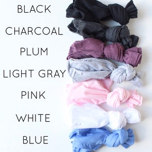 May include: A stack of eight t-shirts in different colors, including black, charcoal, plum, light gray, pink, white, and blue. The t-shirts are folded and tied in a knot.