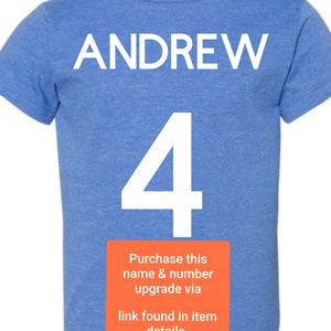 May include: A light blue t-shirt with the name "ANDREW" and the number "4" printed in white. The text "Purchase this name & number upgrade via link found in item details. *not included in price" is printed in white on a red rectangle.