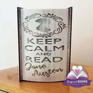 Może przedstawiać: Biała książka w czarnej okładce jest złożona w trójwymiarową rzeźbę. Książka jest ozdobiona czarno-białym wzorem z napisem "Keep Calm and Read Jane Austen".