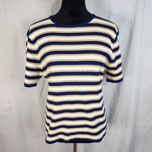 Op de afbeelding: Een gebreide top met korte mouwen en horizontale strepen in marineblauw, crème en goud. De top heeft een ronde halslijn en een iets losse pasvorm. De stof lijkt een zacht, lichtgewicht materiaal te zijn.