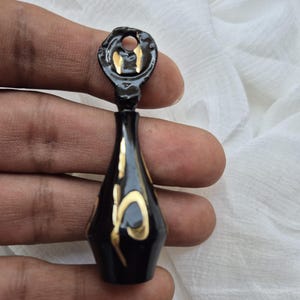 以下が含まれることがあります： 金色のアクセントが付いた黒い装飾的なボトルストッパー。ストッパーは穴のある丸い上部と、細長いボディをしています。金色のアクセントが黒い表面を飾り、装飾的な模様を作り出しています。