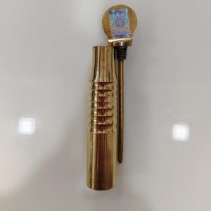 May include: A gold metal pipe with a decorative, ribbed design. The pipe has a removable top with a holographic sticker.