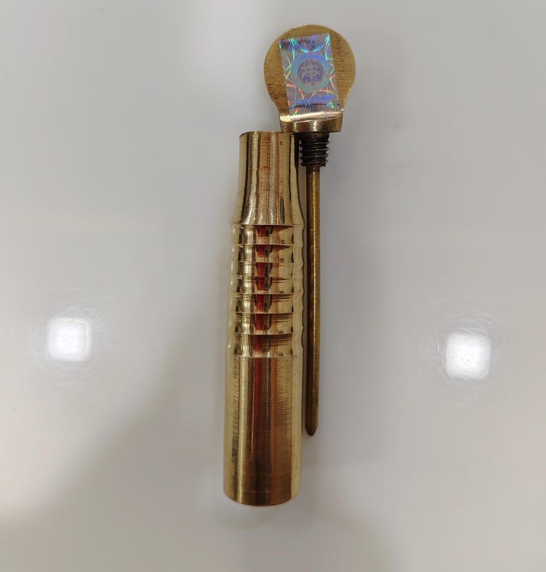 May include: A gold metal pipe with a decorative, ribbed design. The pipe has a removable top with a holographic sticker.