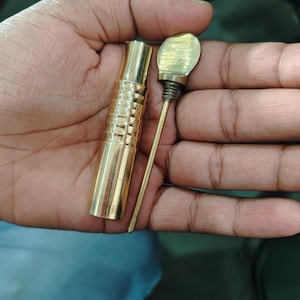 Peut inclure: Un outil en métal doré avec un corps cylindrique et une pointe pointue. L'outil est tenu dans une main.