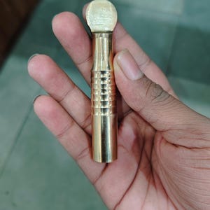 May include: A gold-colored metal tool with a rounded top and a textured, cylindrical body.