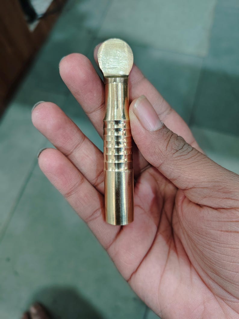 May include: A gold-colored metal tool with a rounded top and a textured, cylindrical body.