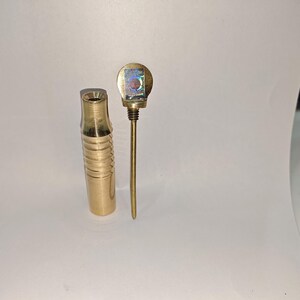May include: A brass smoking pipe with a decorative top and a ribbed body.