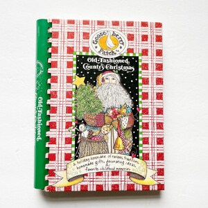 May include: A spiral-bound cookbook titled Old-Fashioned Country Christmas by Gooseberry Patch. The cover features a red and white plaid pattern, a central illustration of Santa Claus holding a small tree and toys, and a yellow banner with text.