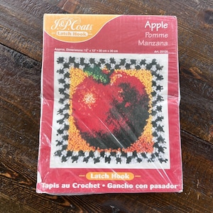 May include: A J&P Coats Latch Hook kit package featuring an apple design. The packaging displays the text Apple, Pomme, Manzana, and Latch Hook, Tapis au Crochet, Gancho con pasador. It lists dimensions of 12 inches by 12 inches and 30 cm by 30 cm.