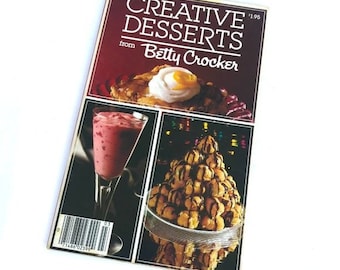Może przedstawiać: Antyczna książka kucharska zatytułowana "Creative Desserts from Betty Crocker" z czerwoną okładką i ceną 1,95 $. Okładka przedstawia trzy zdjęcia deserów: deser z polewą z bezy, szklankę różowego deseru i deser pokryty czekoladą.
