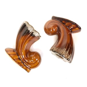 May include: Two brown and white ceramic candle holders shaped like a curled horn. The holders have a glazed finish and a rustic look.