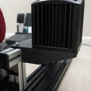 May include: Close-up of a black metal racing simulator frame with a silver aluminum support beam and a black fan mounted on the side.