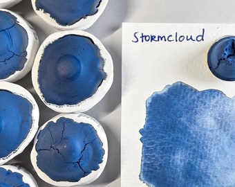 May include: A collection of small blue ink pots with a sample of blue ink on a white card with the text "Stormcloud".