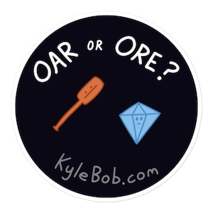 May include: A round sticker with a dark blue background features the text "OAR or ORE?" in white. An orange cartoon oar and a light blue cartoon diamond are also on the sticker. The website KyleBob.com is printed at the bottom.