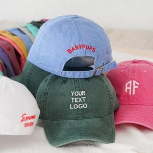 Könnte beinhalten: Baseballkappen in verschiedenen Farben, darunter Blau, Grün und Pink. Die Kappen sind mit Texten wie "BABYPUPS", "YOUR TEXT LOGO", "Emma BRIDE" und Initialen bestickt. Verstellbarer Verschluss mit Metallschnalle.