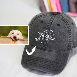 May include: A black washed cotton baseball cap with a white embroidered illustration of a dog holding a stick in its mouth. The text "Mogan" is embroidered on the cap.