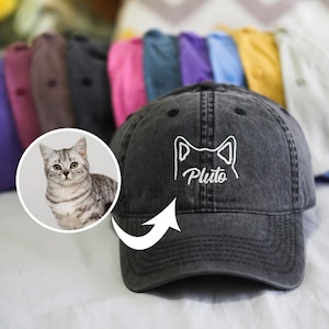 Peut inclure: Une casquette de baseball en denim noir avec une broderie blanche représentant une silhouette de chat et le nom "Pluto".