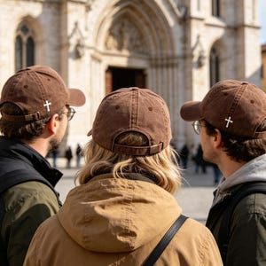 Puede incluir: Tres personas con gorras de b&eacute;isbol marrones con un emblema de cruz blanca. Las gorras tienen una visera curva y una correa ajustable. Est&aacute;n de pie frente a un gran edificio con puertas y ventanas arqueadas.