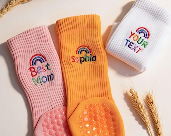 May include: Three ribbed socks in pink, orange, and white, each featuring an embroidered rainbow and custom text. The pink sock reads Best Mom, the orange sock reads Sophia, and the white sock reads YOUR TEXT. Each has grip dots.