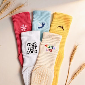 May include: A set of five ribbed crew socks in red, light blue, yellow, white, and cream. The red sock features a white snowflake, the blue a bird, the yellow a mountain, the white reads YOUR TEXT LOGO, and the cream reads PILATES LIFE.