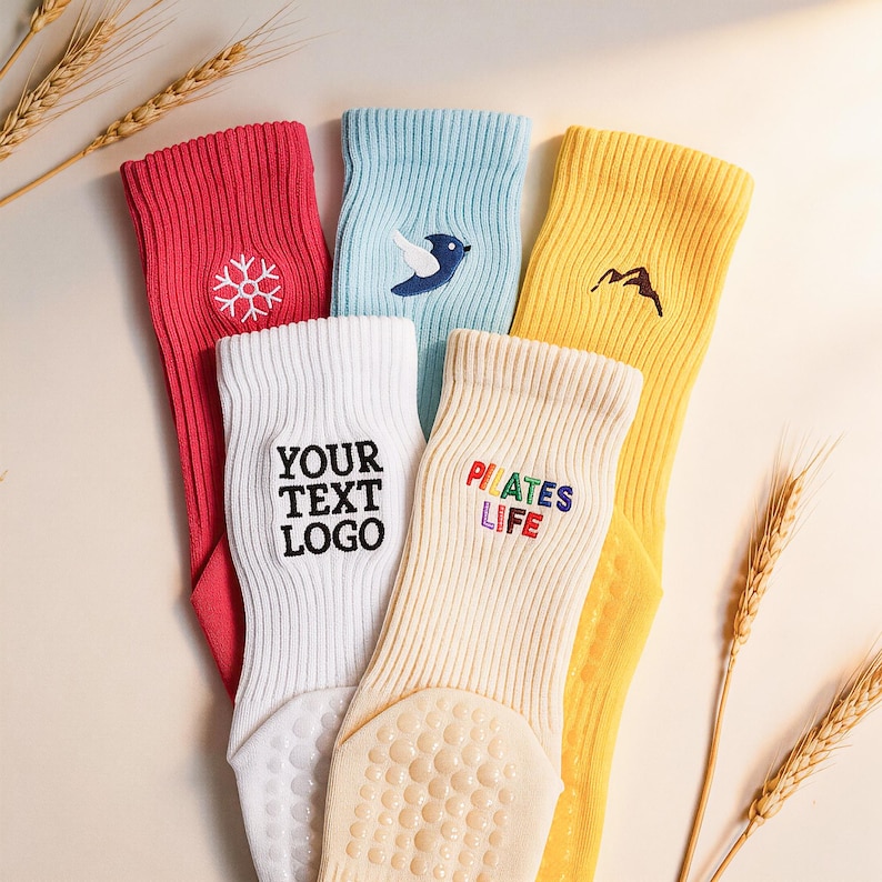 May include: A set of five ribbed crew socks in red, light blue, yellow, white, and cream. The red sock features a white snowflake, the blue a bird, the yellow a mountain, the white reads YOUR TEXT LOGO, and the cream reads PILATES LIFE.