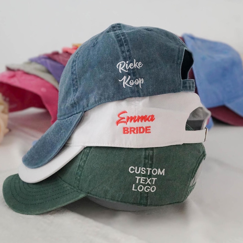 Puede incluir: Una pila de gorras de b&eacute;isbol en varios colores, incluyendo azul vaquero, blanco y verde. La gorra azul vaquero tiene bordado "Rieke Koop" en blanco. La gorra blanca tiene bordado "Emma BRIDE" en rojo. La gorra verde tiene bordado "CUSTOM TEXT LOGO" en blanco.