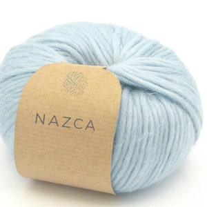 May include: A ball of light blue yarn with a brown paper label. The label has the word "NAZCA" printed in a sans-serif font. The yarn is a soft, fluffy texture, ideal for knitting or crocheting projects.