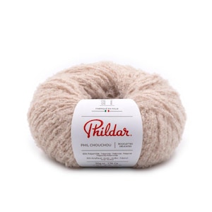 May include: A ball of beige yarn with a white label. The label reads "Phildar PHIL CHOUCHOU BOUCLETTES DELICATES" and lists the fiber content. The yarn ball weighs 50g or 1.76 oz.